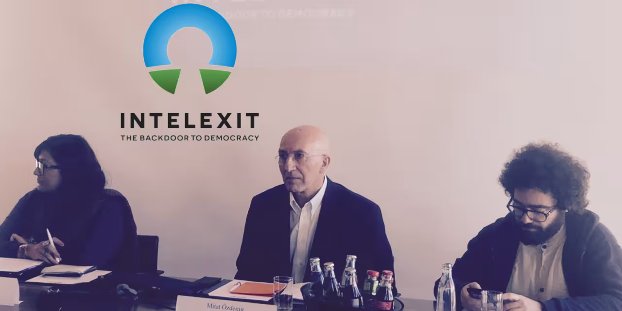 Drei Personen sitzen an einem Tisch während einer Pressekonferenz. Im Hintergrund das Intelexit-Logo.