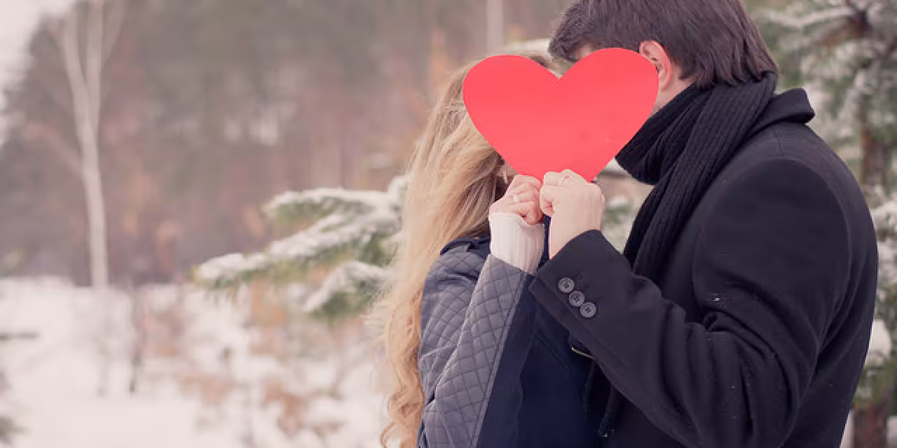 Zwei Personen die sich anscheinend küssen, verdeckt durch ein hochgehaltenes Herz.