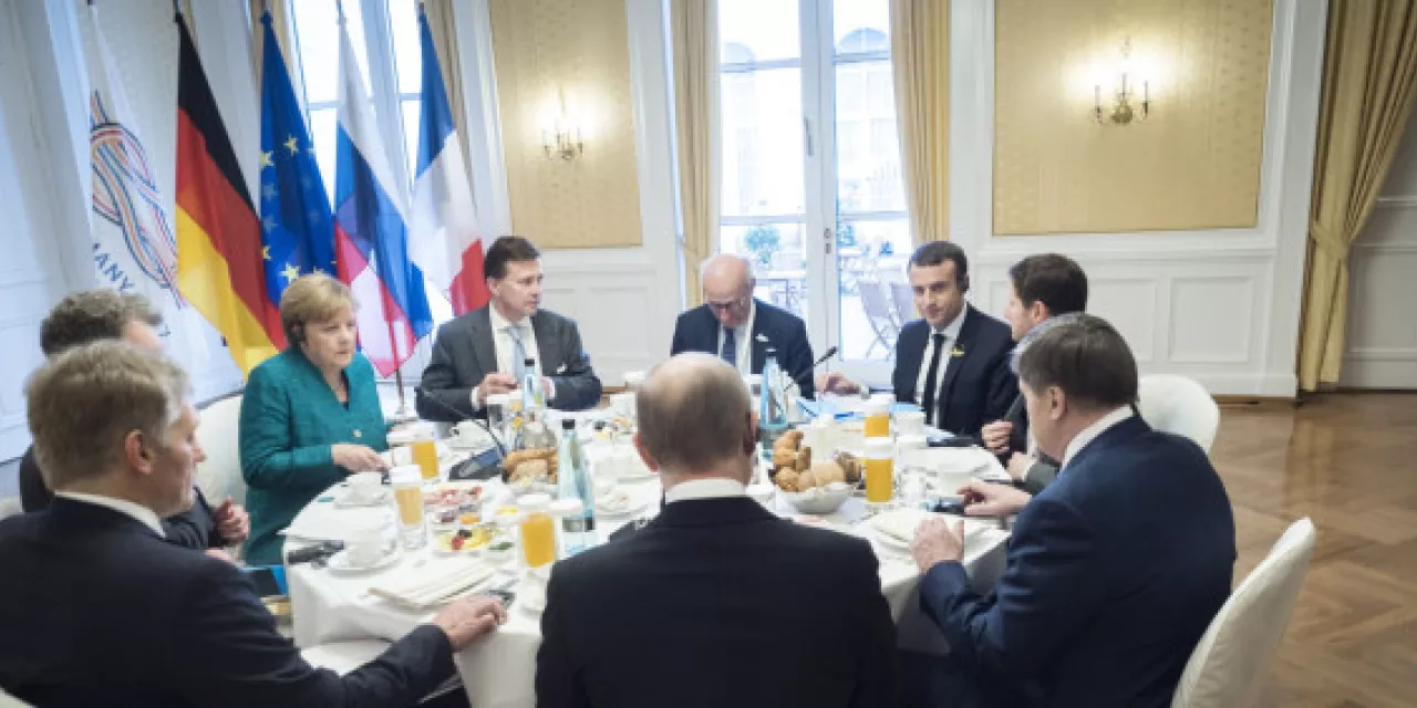 Mehrere Staatschef.innen an einem runden Tisch (u. a. Angela Merkel und Emmanuel Macron).