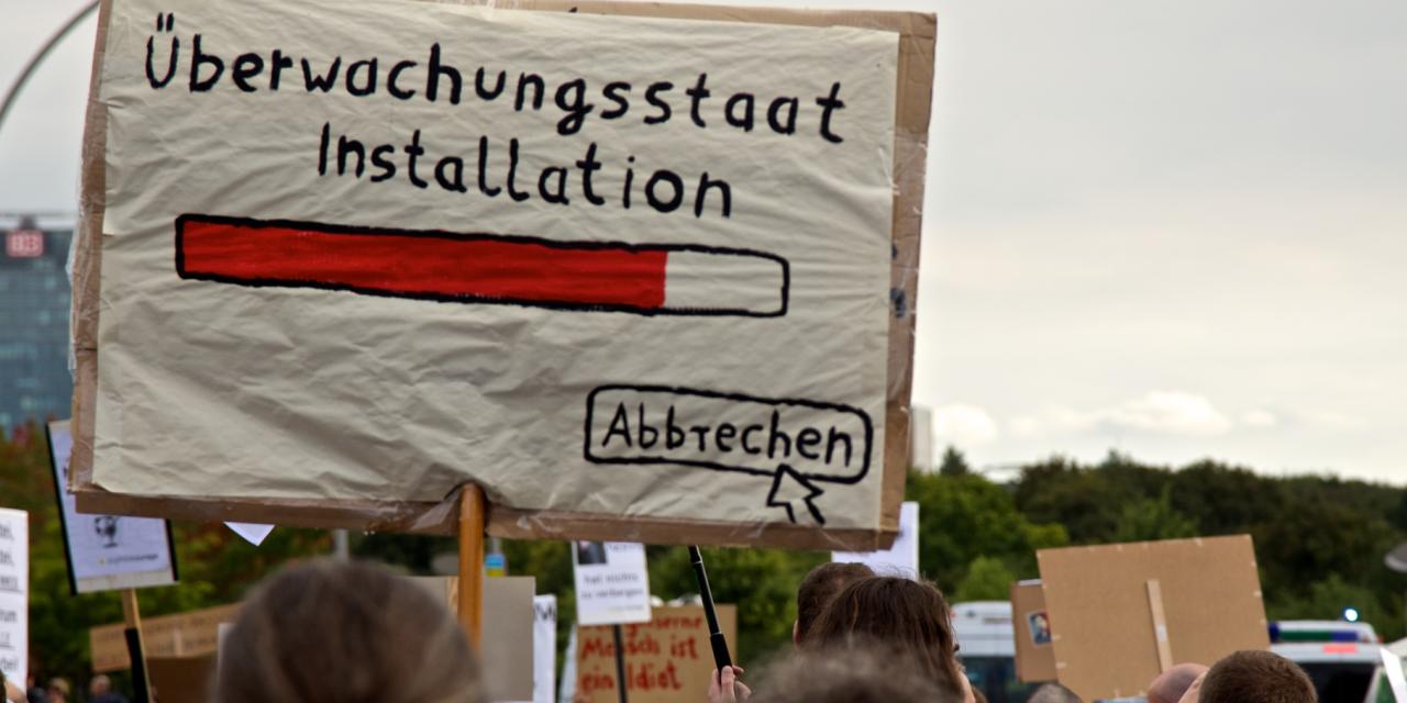 Demoschild mit einem Ladebalken und dem Text „Überwachungsstaat Installation“. Darunter ein Mauszeiger, der auf „Abbrechen“ klickt.